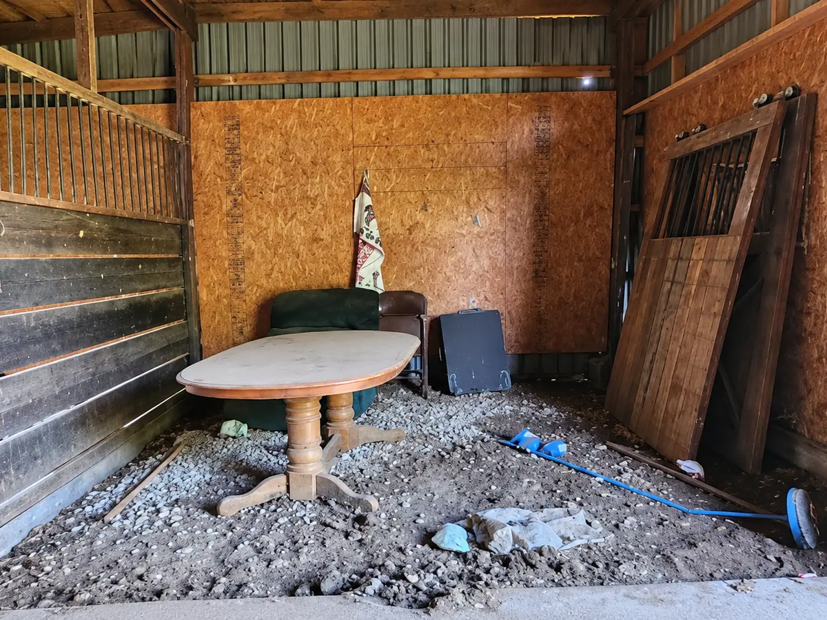 Before: a barn stall with an old table, loose boards and debris on the gravel